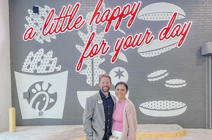 Tyler and Katee Haile standing in front a sign that reads, a little happy for the day