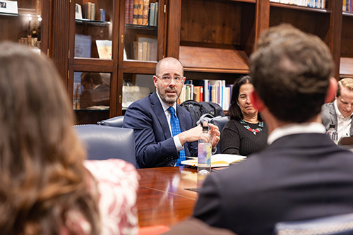 Knox Thames speaking at a conference table during a meeting with bookshelves in the background