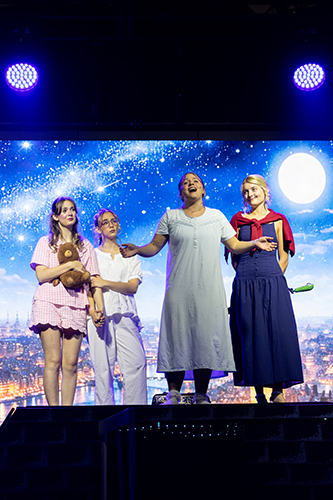 college students on a stage in costume standing in front of a starry night cityscape backdrop