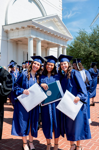 Three graduates smile with diplomas outside Pilgrim Chapel