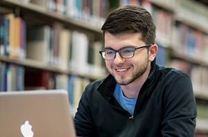 picture of a man wearing glasses smiling at his computer in the library