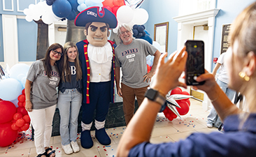 dbu family taking a picture with the Patriot man on campus near the Liberty bell replica