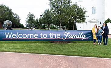 dbu family standing by a sign that reads welcome to the family