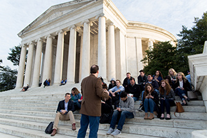 students sitting outside of the Supreme Court building on the steps listening to a professor teach