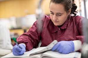 girl in red shirt writing notes in lab journal