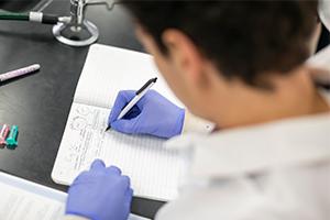 purple gloved hand writing in lab journal with a pen 