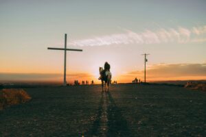 man on donkey with cross in the background