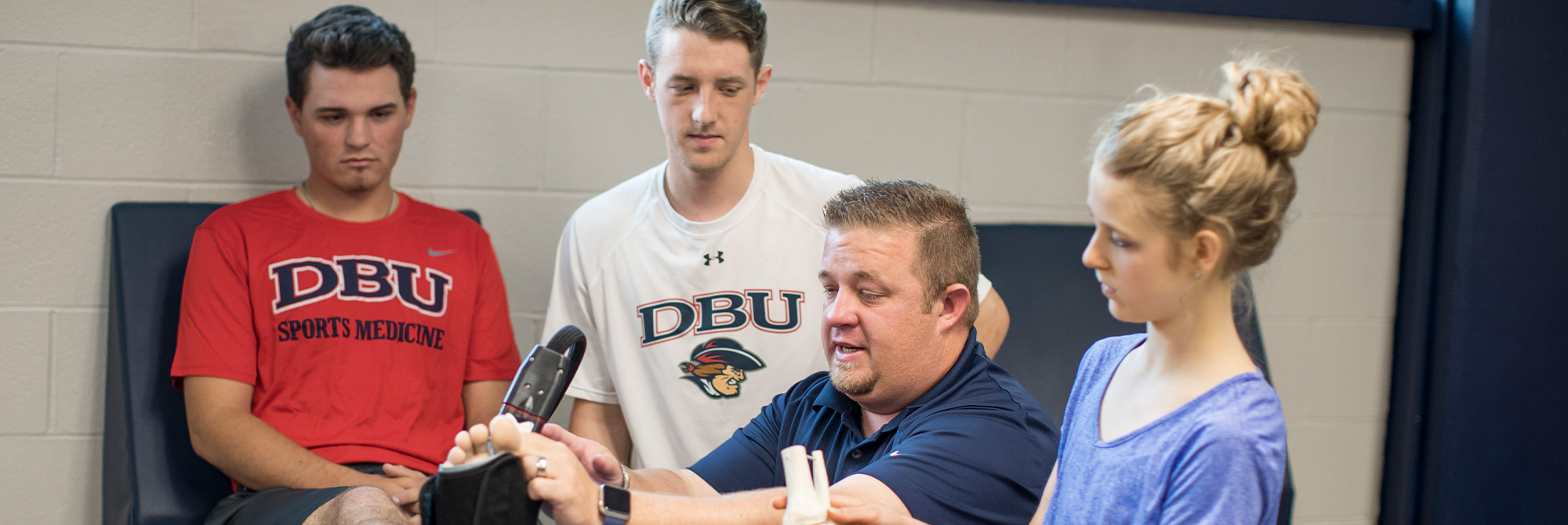 athletic trainer working with athlete while interns watch